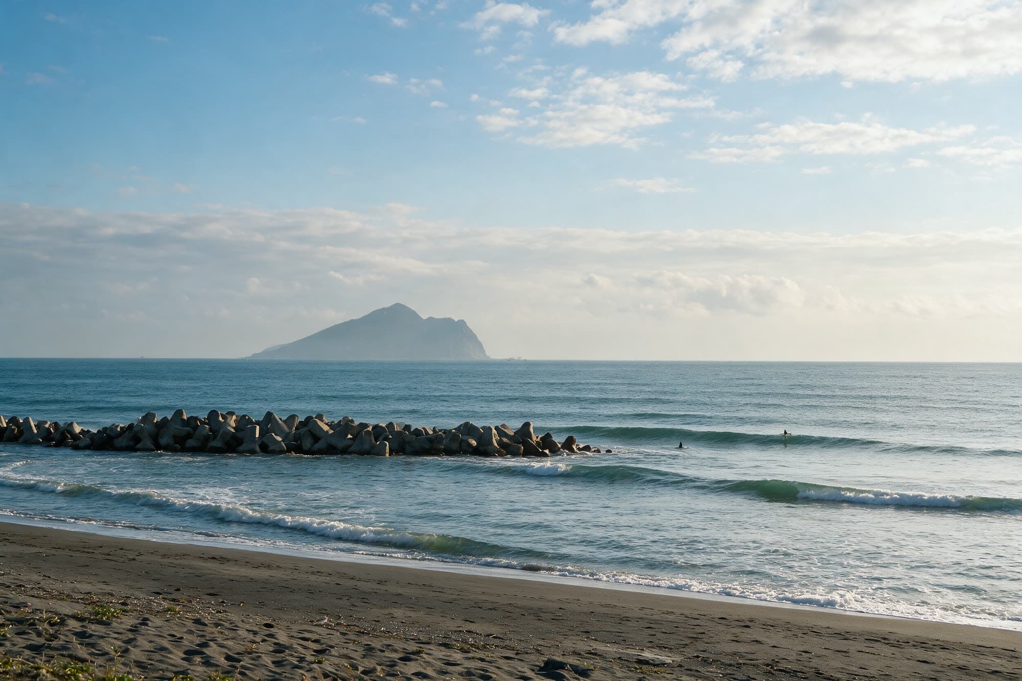 臭水的海灘,一道消波塊堤防延伸到海裡,遠處海面上是龜山島的輪廓,幾位衝浪者在小浪裡