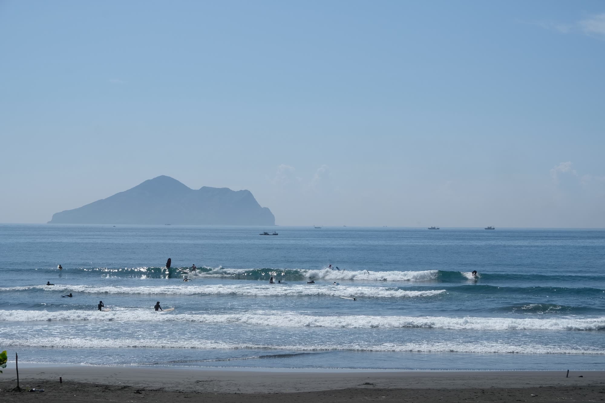 雙獅海灘的黑沙灘,海面上有幾位衝浪者在小浪裡練習,遠處是龜山島的輪廓